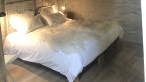 A cozy bedroom with a wooden ceiling, stone walls, a bed with white bedding, and two wall-mounted lamps.