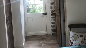 A narrow hallway with a wooden ceiling, a white door with a window, and a wooden cabinet with a floral cushion.