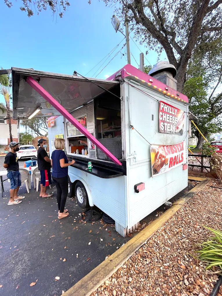 Un camión de comida con toldo rosa y un cartel que anuncia sándwiches de queso y langosta.