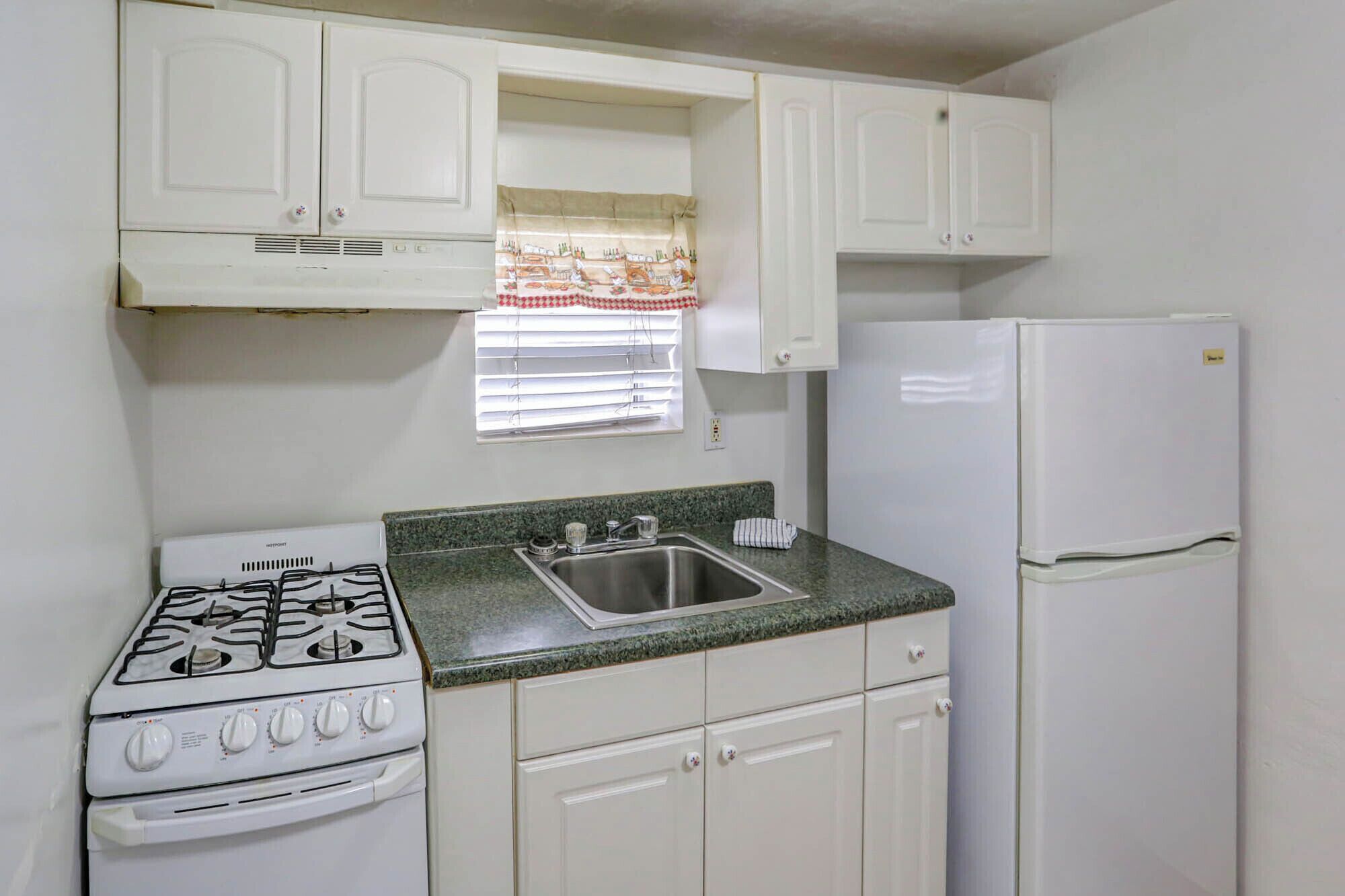 A compact kitchen with white cabinets, a gas stove, a sink, and a refrigerator.