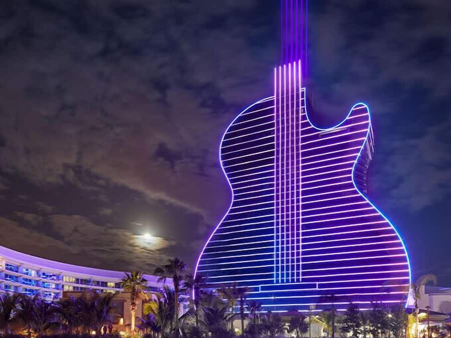 A large building with a guitar-shaped design, illuminated with purple and blue lights.