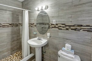 A bathroom with a shower, sink, toilet, and a mirror.