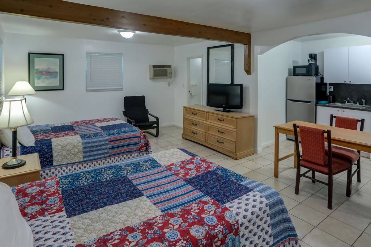 A room with two beds, a TV, a wooden dresser, a desk, and a chair.