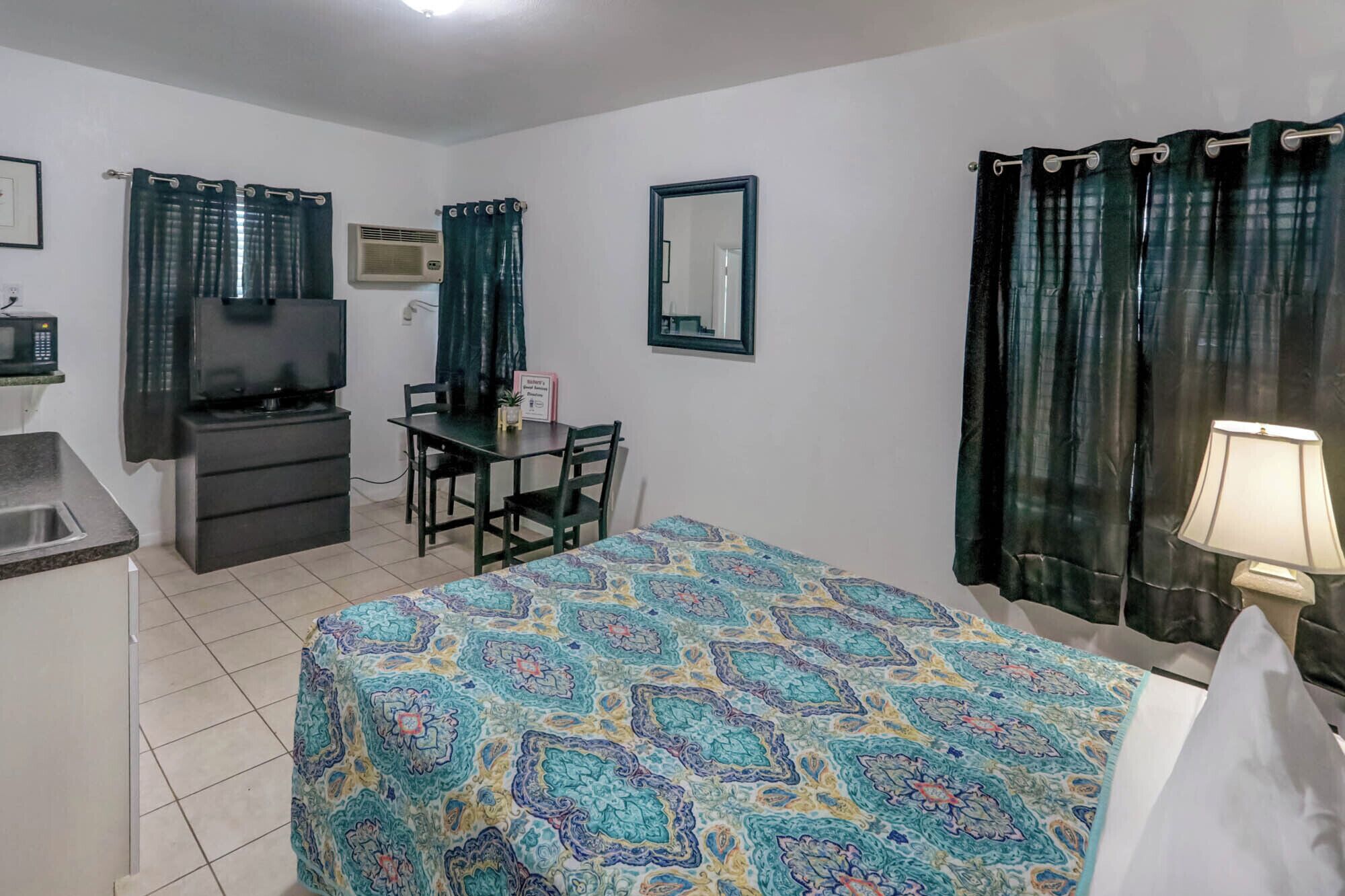 Ein Hotelzimmer mit Bett, Schreibtisch, Stuhl, Fernseher, Spiegel und Lampe.