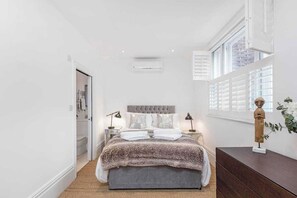 Une chambre à coucher avec un lit, des tables de chevet, une commode et une fenêtre avec des stores.