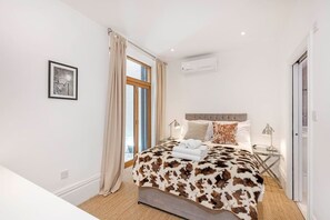Une chambre avec un grand lit, une fenêtre avec des rideaux, un tableau encadré au mur et un appareil de climatisation.