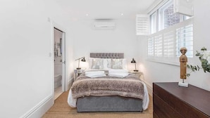 A bedroom with a large bed, bedside lamps, a dresser, and a window with blinds. - Fulham Broadway 2-bed Apt w/ Garden & Pets Ok (London)