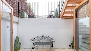 A courtyard with a metal bench, a small potted plant, and a staircase leading to an upper level. - Fulham Broadway 2-bed Apt w/ Garden & Pets Ok (London)