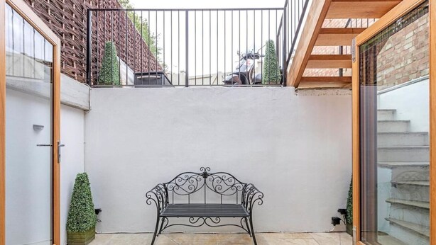 Un patio con un banco de metal, una pequeña planta en maceta y una escalera que lleva a un nivel superior.