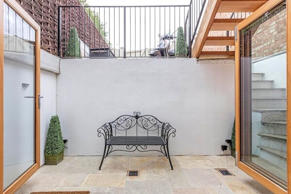 Une cour avec un banc en métal, une petite plante en pot et un escalier menant à un niveau supérieur.