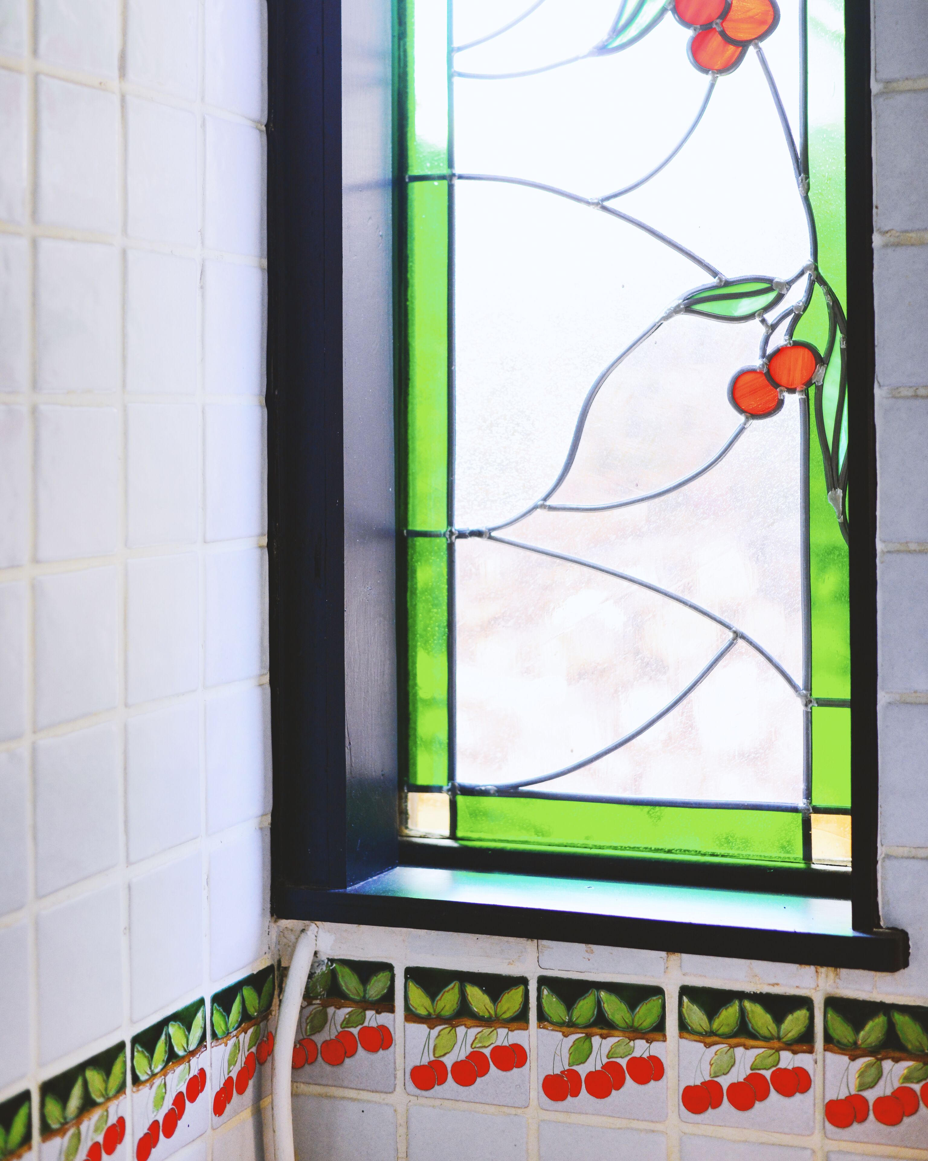 Una finestra con vetri colorati raffigurante un disegno floreale e una cornice piastrellata con motivi di frutta.