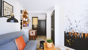 Un salon avec un canapé gris, un coussin orange, une table d’appoint en bois sur laquelle se trouve une plante, et une lampe noire.