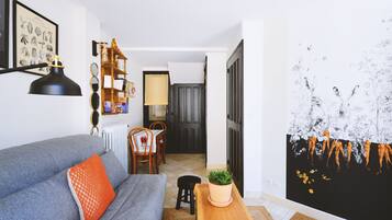 Un salon avec un canapé gris, un coussin orange, une table d’appoint en bois sur laquelle se trouve une plante, et une lampe noire.