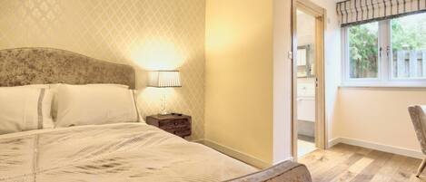 A bedroom with a large bed, a nightstand with a lamp, a chair, and a window with a view of the outside.