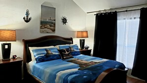 Une chambre à coucher avec un lit agrémenté de linge de lit sur le thème de la marine, une horloge murale et un tableau représentant un phare.