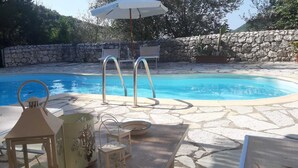 A pool area with stone flooring, lounge chairs, a table, and a decorative lantern. - Villa Skorpios (lefkada)