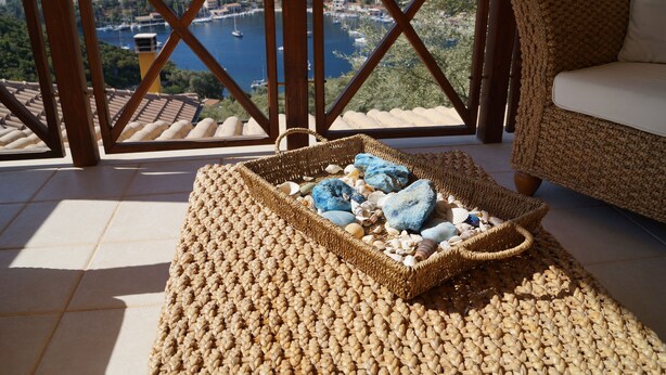 A wicker basket filled with stones on a woven mat, with a view of a marina and boats through a wooden railing. - Villa Skorpios (lefkada)