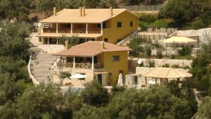 A two-story yellow building with a balcony, surrounded by trees and a stone wall. - Villa Skorpios (lefkada)