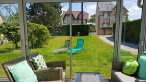A sunlit patio with wicker furniture and a glass door leading to a grassy yard. - Cocooning bubble and immersive veranda in a green setting 100m from the beach (Varaville)