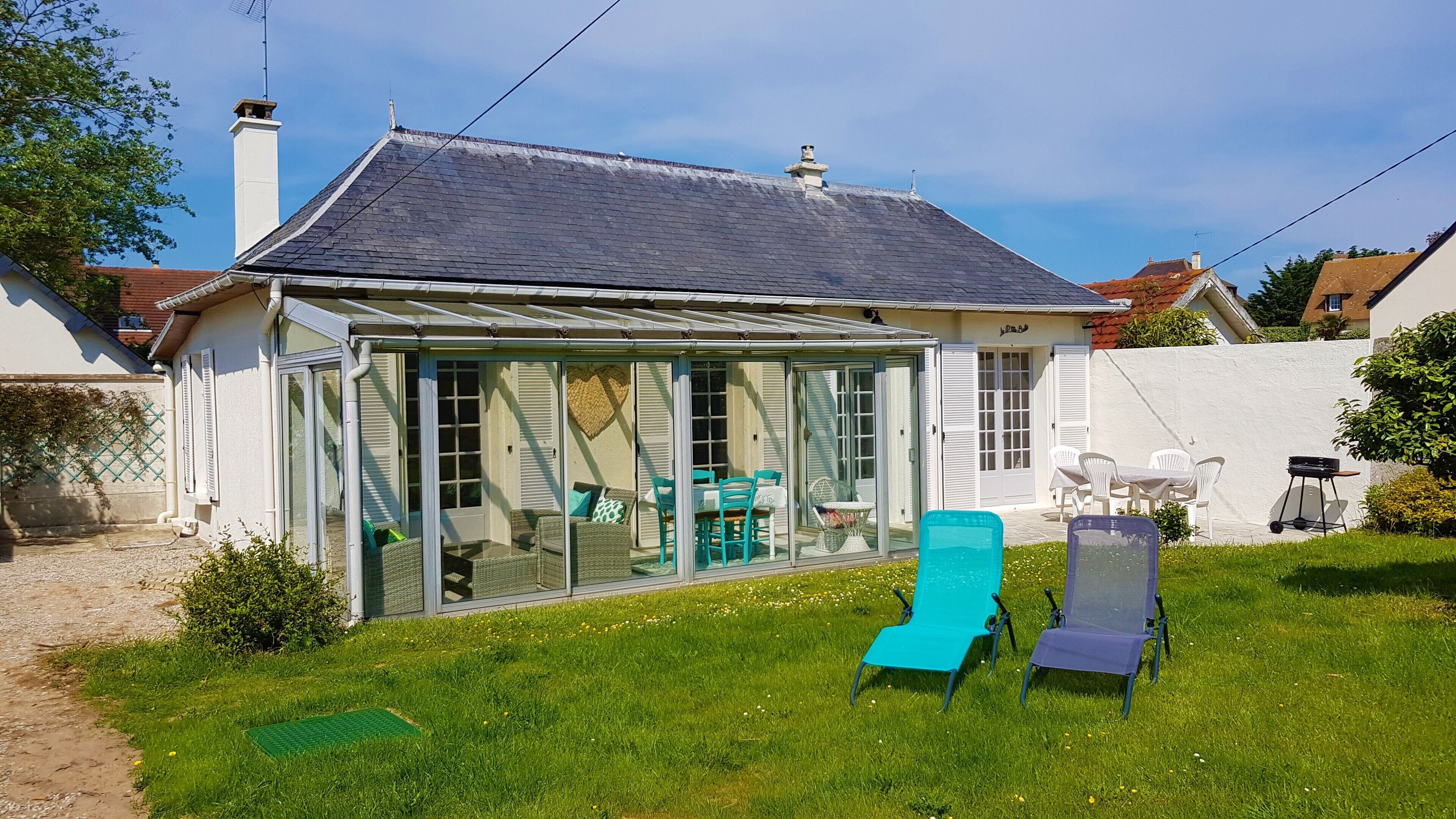 Une maison dotée d’un patio entièrement vitré, d’une façade blanche et d’un toit gris.