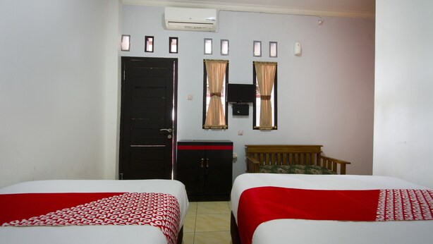 A hotel room with two beds, a wardrobe, a television, and a door. - OYO 3126 Penginapan Suka Asih (Pangandaran)