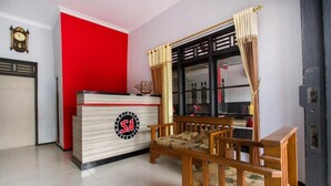 A reception area with a red wall, a reception desk, a wooden bench, and a window with curtains. - OYO 3126 Penginapan Suka Asih (Pangandaran)