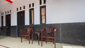 A room with three wooden chairs and a small table, a black door with a number, and a window with curtains. - OYO 3126 Penginapan Suka Asih (Pangandaran)