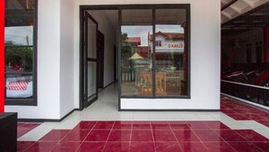 A modern building with a glass entrance, a tiled floor, and a visible sign in the background. - OYO 3126 Penginapan Suka Asih (Pangandaran)