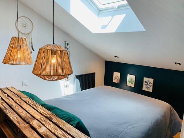 A modern bedroom with a skylight, a large bed, two hanging rattan lamps, and a wooden bench.