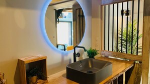 Een badkamer met een ronde spiegel, een houten wastafelmeubel en een zwarte wasbak.