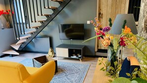 Een moderne woonkamer met een trap, een flatscreen televisie, een gele bank, een kamerkleed met patroon en een bloemstuk.
