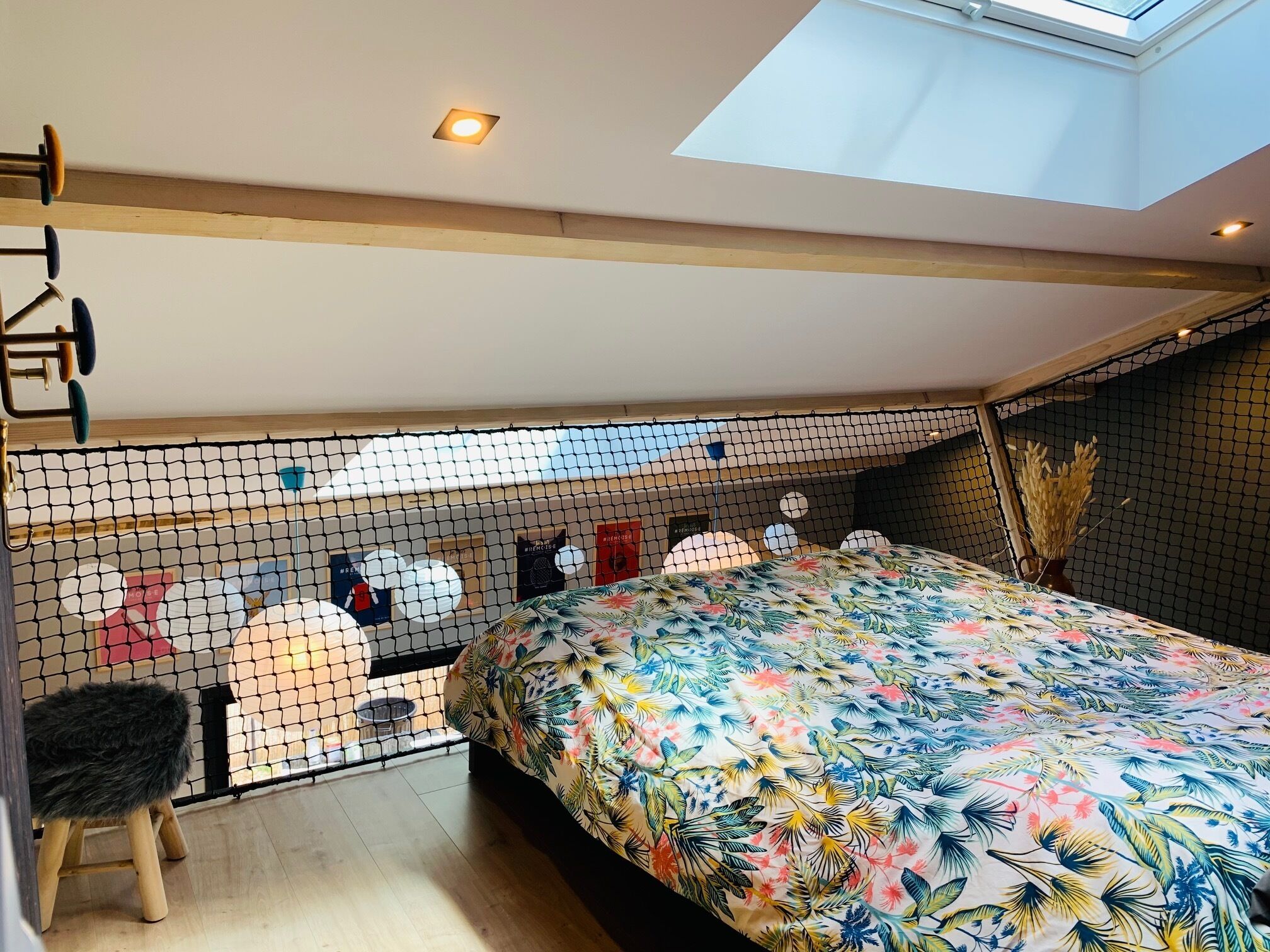 A bedroom with a sloped ceiling, a skylight, a bed with a floral bedspread, a small stool, and a netted partition.