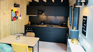Een kleine keuken met donkere kastjes, een magnetron, een koffiezetapparaat en een spoelbak.
