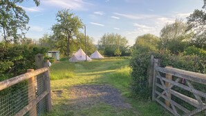 A campsite with three tents, a wooden gate, and a grassy path leading to the tents. - Glamping at The Homestead - Ensuite Bell Tent (Hereford)
