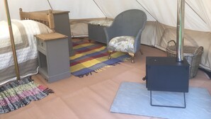 A tented accommodation with a bed, a chair, a small table, and a basket. - Glamping at The Homestead - Ensuite Bell Tent (Hereford)
