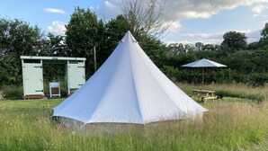 A tent in a grassy field with a picnic table and a small building in the background. - Glamping at The Homestead - Ensuite Bell Tent (Hereford)