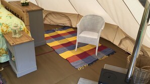 A tent with a wicker chair, a colorful rug, and a portable stove.
