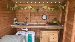 A compact wooden cabin with a kitchenette, a table with a polka dot tablecloth, and a green chair.