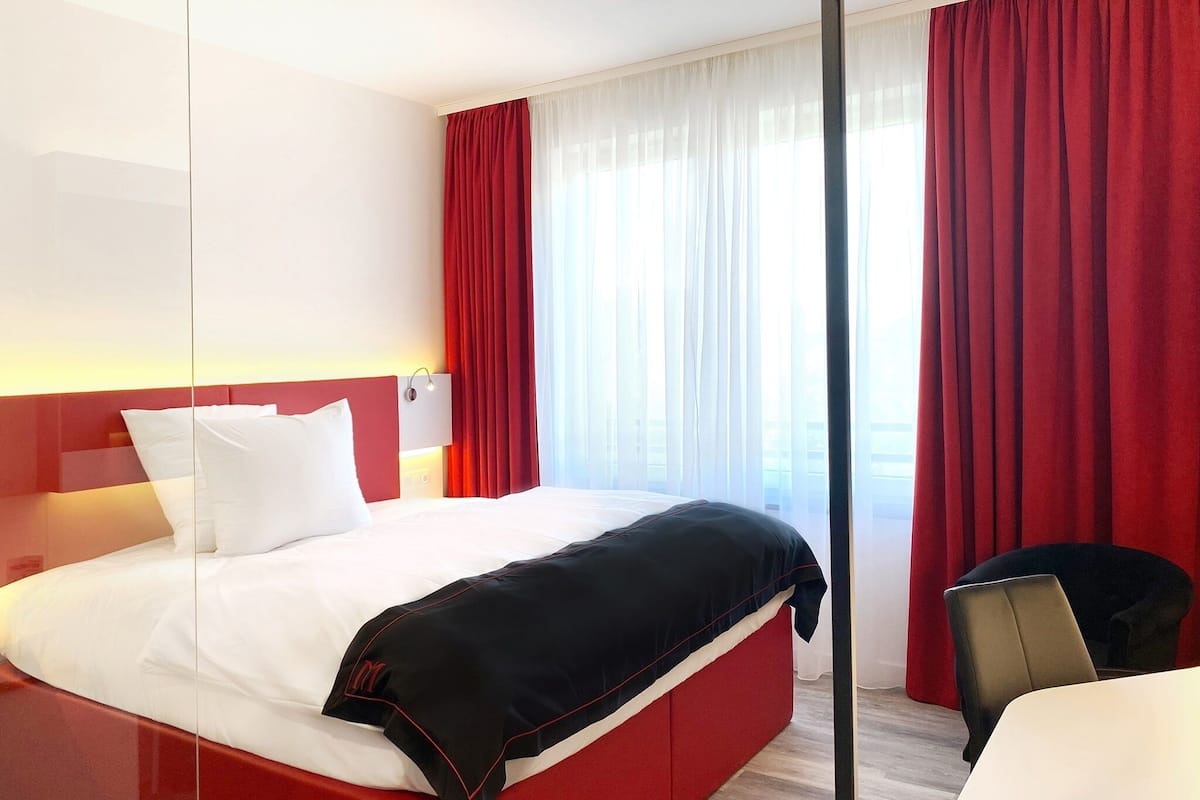 Habitación de hotel con una cama grande, cortinas rojas y vistas a la ciudad.