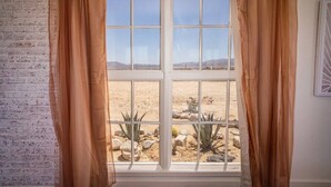 A room with a large window, white curtains, a brick wall, and a view of a desert landscape.