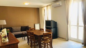 A living room with a sofa, a dining table with chairs, a TV on a stand, and an air conditioner. - Gorgeous apartment with large sea view terrace (Civezza)