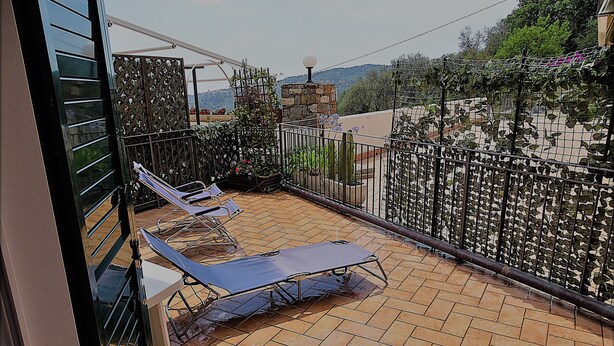 A balcony with sun loungers, a stone wall, and a view of a hilly landscape. - Gorgeous apartment with large sea view terrace (Civezza)