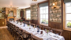 A long dining table set for a meal in a room with large windows, wooden walls, and a brick fireplace.