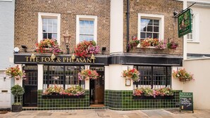 A pub named "The Fox & Pheasant" with a brick facade, hanging flower baskets, and a green signboard.