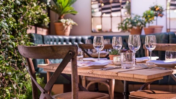 A wooden table set for dining with empty wine glasses, plates, and cutlery.