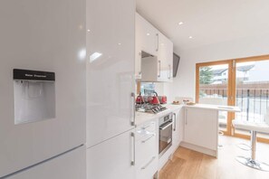 Une cuisine moderne avec des meubles blancs, un distributeur d’eau, une cuisinière et une grande fenêtre donnant sur l’extérieur.