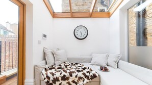 A cozy corner with a white sofa, a cowhide blanket, and a clock on the wall.