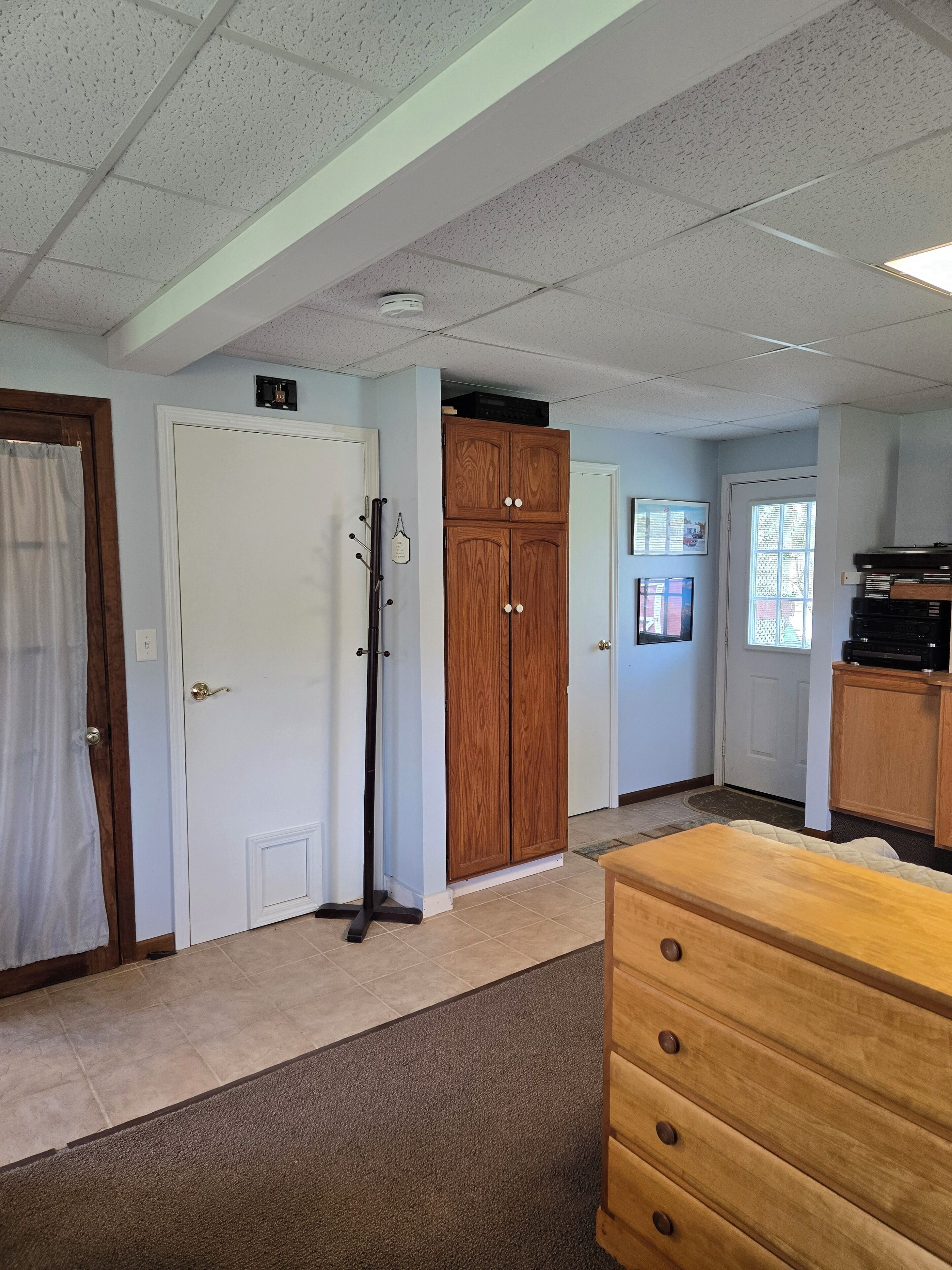 A room with a wooden cabinet, a white door, a coat rack, and a window.