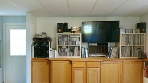 A home entertainment room with a large flat-screen TV, wooden cabinets, and shelves filled with books and CDs. - A quiet place near Ithaca, Ithaca College & Cornell. (Danby)