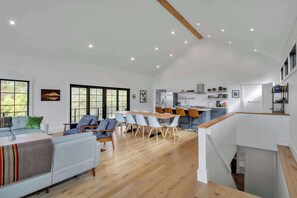 Amplia sala de estar con una mesa de comedor y sillas, una cocina al fondo y ventanas grandes.